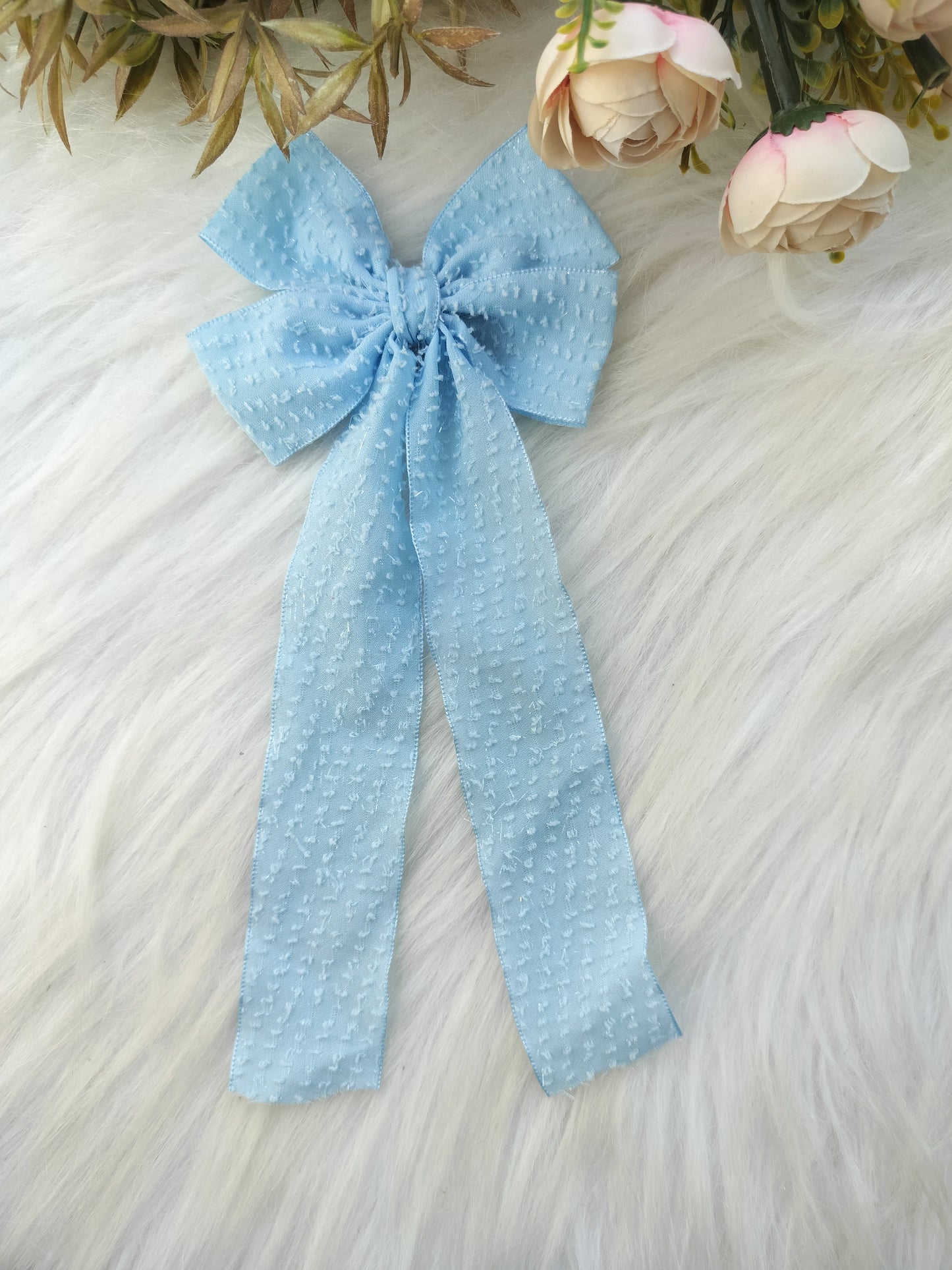 Light blue polka dot bow on a textured surface with flowers in the background