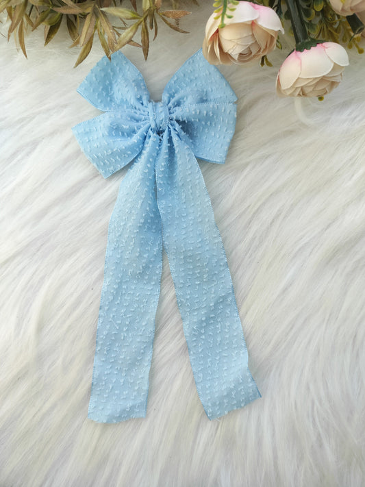 Light blue polka dot bow on a textured surface with flowers in the background